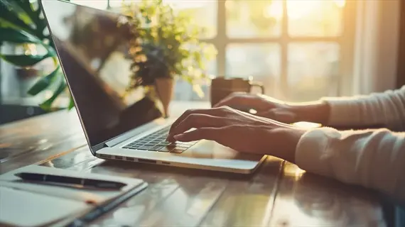 concentrating morning work: hands typing on laptop at sunlit wooden desk with coffee mug and potted plant, enhancing cognitive function through focused work