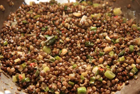 cooked lentils with chopped herbs and diced vegetables in a pan