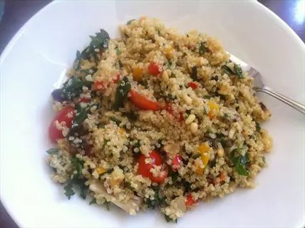 cooked quinoa bowl: fluffy quinoa grains mixed with cherry tomatoes, herbs, and pine nuts in a white dish, fork resting on the side