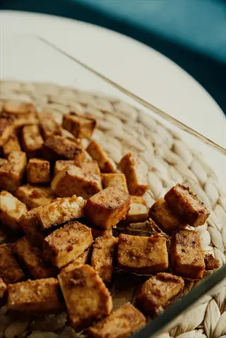 cooked tofu portion: golden-brown cubed tofu in glass dish on woven placemat