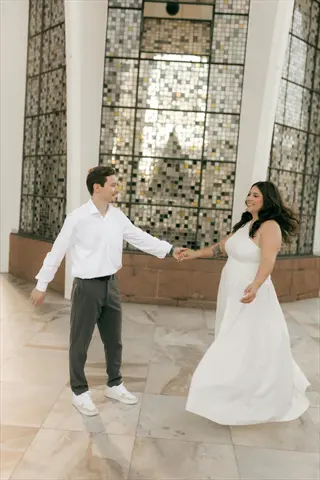 couple dancing indoors in formal wear holding hands before decorative glass wall