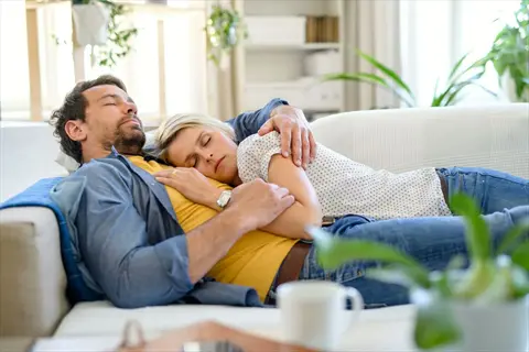 couple resting on a living room couch during a bedtime relaxation routine - pre-sleep transition with soft natural light
