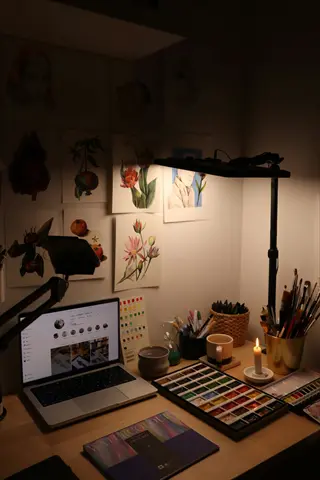 cozy art workspace with laptop, watercolor paints, brushes and botanical sketches set up for an office painting session or art therapy workshop