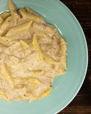 creamy nutritional yeast pasta with penne in a teal bowl on wooden surface
