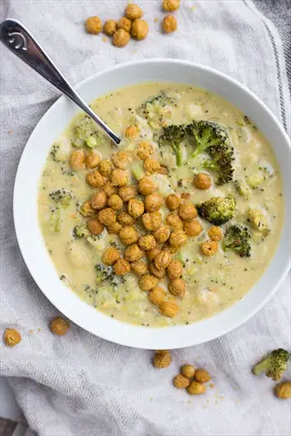 creamy nutritional yeast soup with broccoli florets and roasted chickpeas in white bowl, garnished with extra chickpeas on textured linen cloth