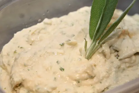 creamy white bean spread in a glass container, garnished with fresh sage leaves