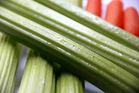 crisp fresh celery stalks with visible ridges, background carrots