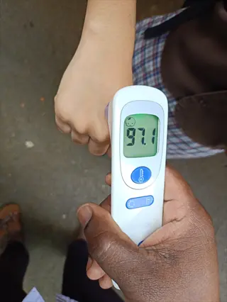 digital thermometer checking wrist temperature (97.1°f) with gloved hand holding device against blurred background
