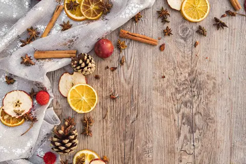 diy cinnamon potpourri ingredients arranged on wooden surface: cinnamon sticks, dried orange slices, star anise, pinecones, and fabric; aromatic home freshener display