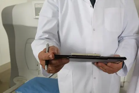 doctor in white lab coat holding clipboard and pen near sleep study equipment, representing professional consultation for sleep disorders