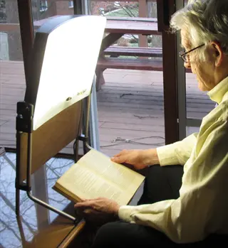 elderly person using light therapy lamp for depression treatment while reading a book near a sunlit window