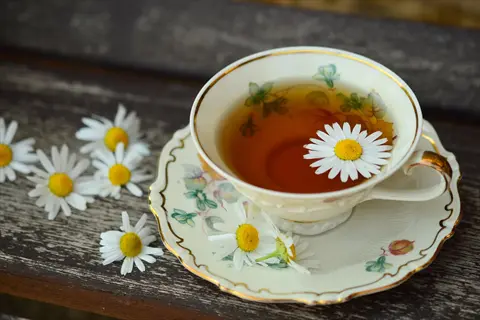 elegant chamomile tea cup with floating flower, vintage saucer, and scattered blooms on rustic wooden surface