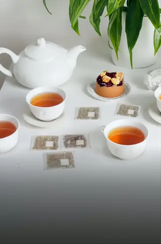 elegant tea setting with white teapot, multiple cups of herbal tea, tea bags, and a dessert, illustrating herbal tea hydration
