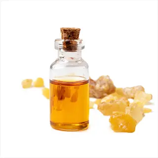 essential oil frankincense bottle with cork stopper containing golden liquid, surrounded by natural frankincense resin pieces on white background