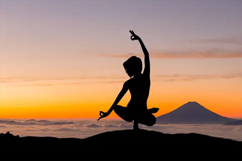 evening meditation: silhouette of a person in yoga mudra pose against a vibrant sunset sky with mount fuji and cloud layers in the background
