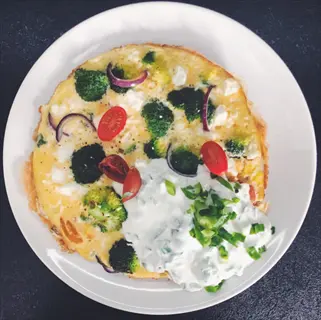 feta cheese omelet with broccoli, cherry tomatoes, red onions, and herbed yogurt on white plate