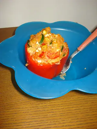 feta-stuffed red bell pepper in a blue flower-shaped bowl with fork on wooden table