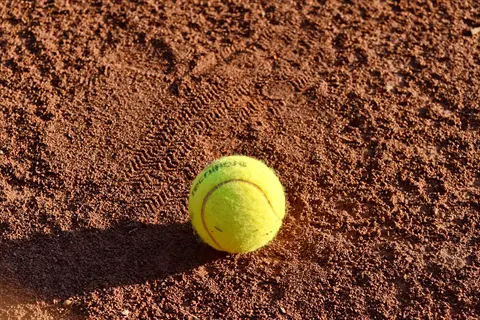 foot tennis ball: yellow tennis ball on a clay court with surrounding footprints, used in soccer footwork drills or foot massage techniques