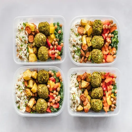 four plastic containers showcasing a healthy food variety: veggie balls, rice, roasted vegetables, chickpeas, and leafy greens arranged in neat portions