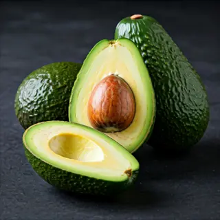 fresh avocado fruits: whole green-skinned avocados and one halved to reveal pit with creamy flesh, on dark surface