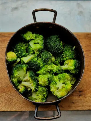 fresh broccoli florets in a rustic metal pot with handles on a wooden surface