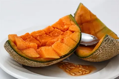 fresh cantaloupe melon slices cut into cubes with seeds and spoon on white plate