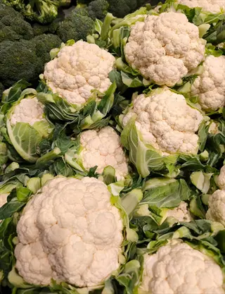 fresh cauliflower heads with creamy-white florets and green leaves piled together