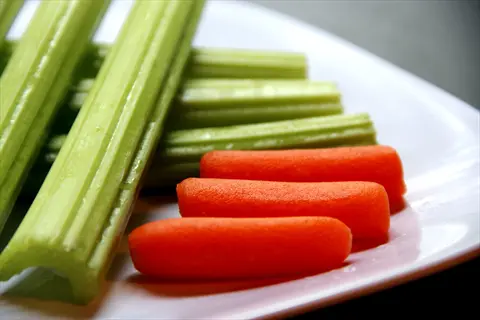 fresh celery stalks and baby carrots arranged on a white plate with a dark background