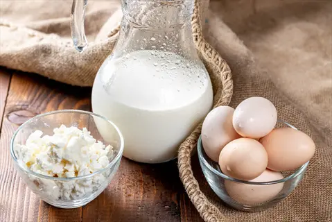 fresh eggs in a glass bowl, milk in a pitcher, and cottage cheese on a rustic wooden table with burlap