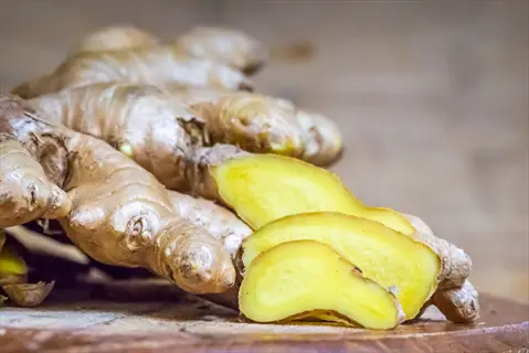 fresh ginger root with sliced pieces showing vibrant yellow interior on rustic wooden surface