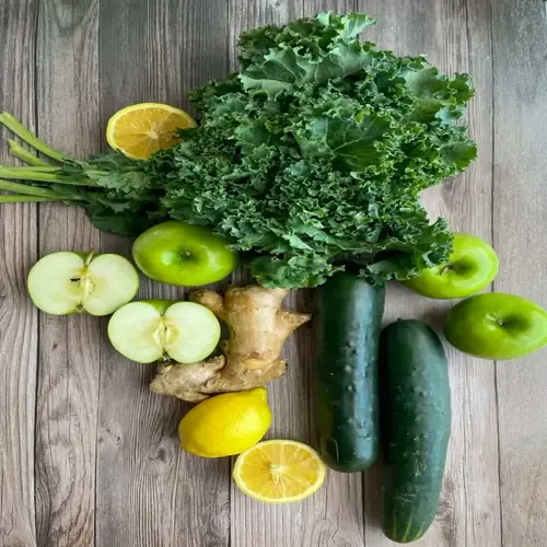 fresh kale spinach green juice ingredients: curly kale, green apples, lemons, ginger root, and cucumbers arranged on rustic wooden background