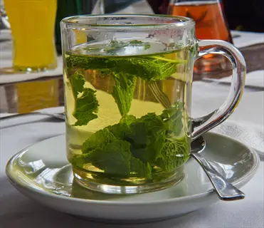 fresh peppermint tea in glass cup with vibrant leaves on table setting