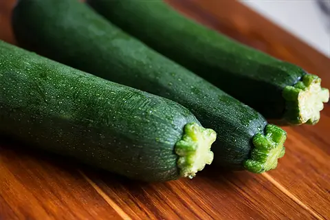fresh zucchini vegetables with dewy dark green skin and ridged ends on wooden surface