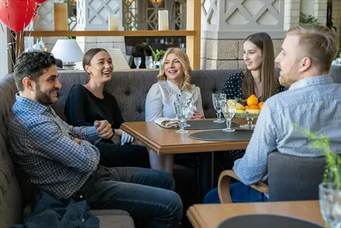 friends cafe talking: group of five people laughing and conversing at a restaurant table with glasses and fruit bowl