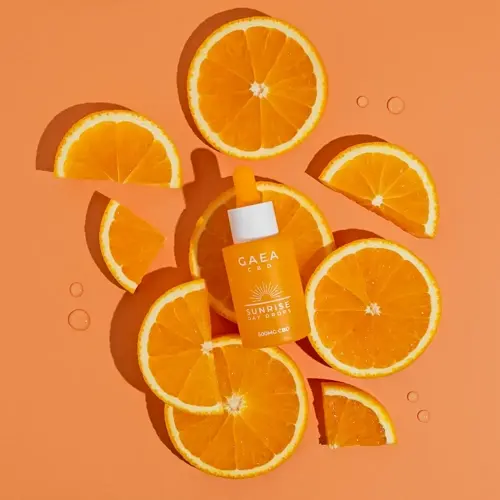gaea cbd sunrise day drops bottle surrounded by fresh orange slices and glistening water droplets, evoking orange essential oil drops for wellness