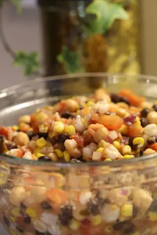 glass bowl of black bean dip with corn, tomatoes, and mixed beans, background features ivy in a golden container