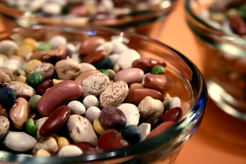 glass bowls filled with colorful mixed beans: kidney beans, chickpeas, pinto beans, and lentils on orange background