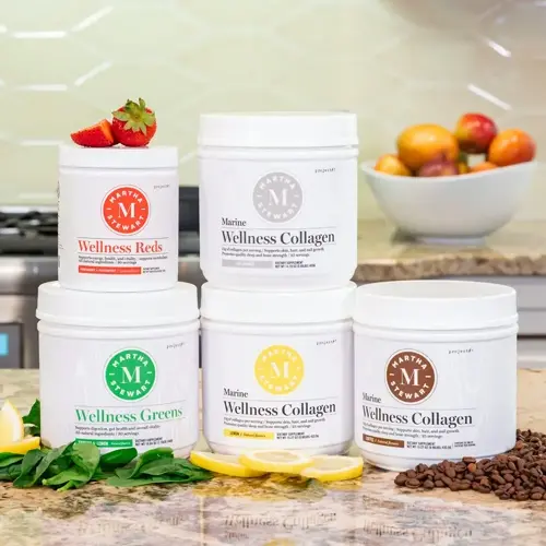 glass containers of marine wellness collagen powder, wellness reds, and wellness greens supplements on a kitchen counter with fruits and coffee beans