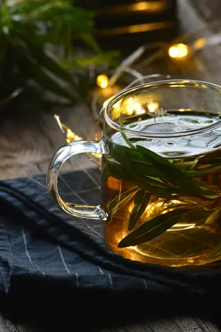glass herbal tea cup with fresh green leaves, resting on dark cloth amidst warm fairy lights for cozy evening relaxation