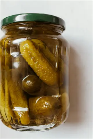 glass jar of fermented pickles in brine with green lid, showcasing probiotic preservation
