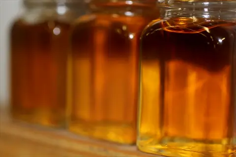 glass jars filled with amber liquids: honey, maple syrup, or other natural sweeteners arranged on a wooden surface