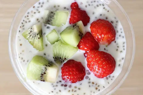 glass of creamy yogurt with chia seeds, topped with fresh kiwi slices and strawberries for a healthy snack