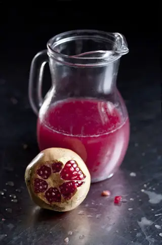 glass pitcher of red juice (pomegranate) with whole pomegranate fruit, highlighting cranberry juice antioxidants (polyphenols) in vibrant beverage presentation