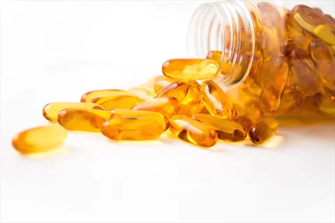 golden fish oil capsules spilling from clear bottle onto white surface, typical omega-3 supplement softgels