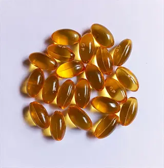 golden oval garlic supplement capsules scattered on white background, typical softgel form for odorless garlic supplements