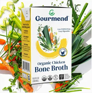 gourmend organic chicken bone broth carton surrounded by fresh vegetables (carrots, celery, leeks) - ready-to-heat hot bone broth drink base