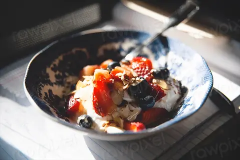 greek yogurt bowl with fresh strawberries, blueberries, and almond slivers in blue patterned dish on notebook with visible text