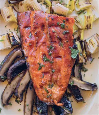 grilled salmon fillet cooked and served with sautéed mushrooms, leeks, and fresh herbs on a plate