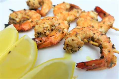 grilled shrimp skewers with herbs and lemon wedges on white plate