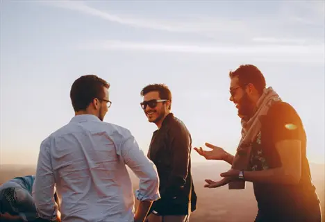 group of friends laughing together outdoors at sunset, three men in casual clothing sharing joyful moment with open body language and warm lighting